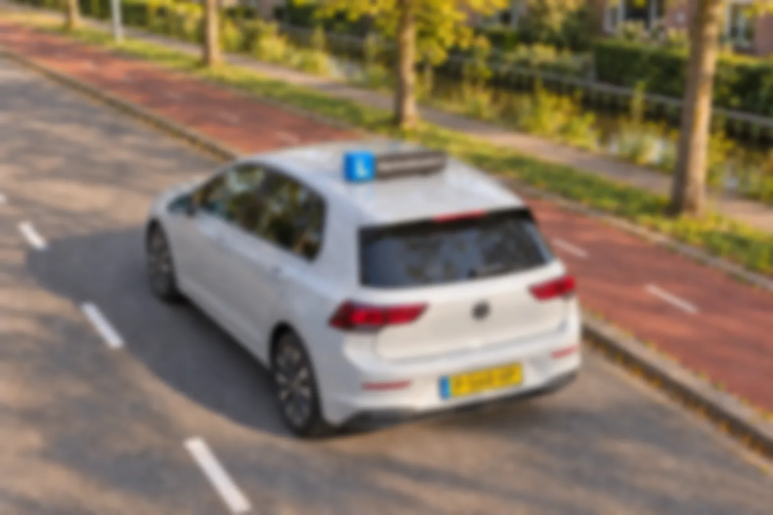 Witte Volkswagen Golf lesauto met dakbord Rijschooldaoudi.nl op een straat langs een gracht