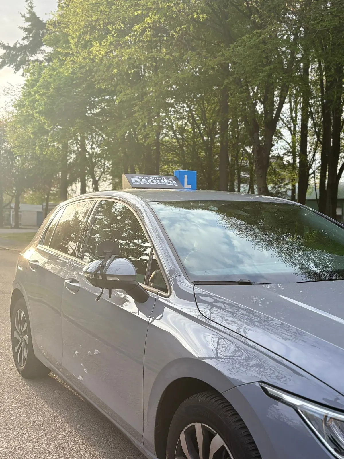 Zijkant van de grijze Volkswagen Golf lesauto met dakbord van Rijschool Daoudi